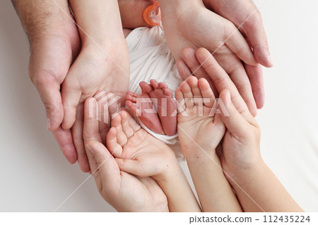 The palms of the father, the mother are holding the foot of the newborn baby in a white blanket. Feet of the newborn on the palms of the parents. Studio macro photo of a child's toes, heels and feet. The palms of the father, the mother are holding the foot of the newborn baby in a white blanket. Feet of the newborn on the palms of the parents. Studio macro photo of a child's toes, heels and feet. 112435224