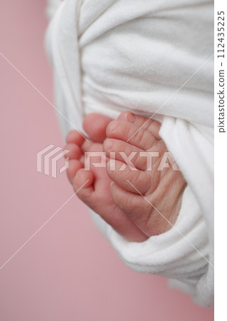 The tiny foot of a newborn baby. Soft feet of a new born in a white blanket. Close up of toes, heels and feet of a newborn. Macro photography on the pink background. The tiny foot of a newborn baby. Soft feet of a new born in a white blanket. Close up of toes, heels and feet of a newborn. Macro photography on the pink background. 112435225