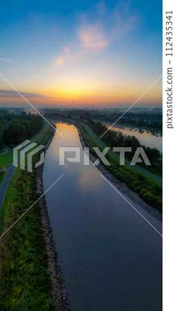 Dawn's Reflection: Sunrise over a Calm Canal Dawn's Reflection: Sunrise over a Calm Canal 112435341