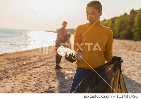 Earth day. Volunteers activists team collects garbage cleaning of beach coastal zone. Woman puts plastic bottle trash in garbage bag on ocean shore. Environmental conservation coastal zone cleaning Earth day. Volunteers activists team collects garbage cleaning of beach coastal zone. Woman puts plastic bottle trash in garbage bag on ocean shore. Environmental conservation coastal zone cleaning 112435450
