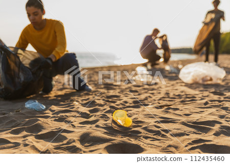 Earth day. Volunteers activists collects garbage cleaning of beach coastal zone. Woman mans with trash in garbage bag on ocean shore. Environmental conservation coastal zone cleaning. Blurred image Earth day. Volunteers activists collects garbage cleaning of beach coastal zone. Woman mans with trash in garbage bag on ocean shore. Environmental conservation coastal zone cleaning. Blurred image 112435460