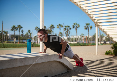 Sportsman doing push ups on stone bench in the city promenade 112435508