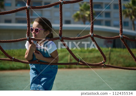 Adorable preschool girl have fun in adventure park. Child on tree top net trampoline. Outdoor activities for small kids 112435534