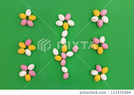 Easter card. Frame of delicious chocolate eggs arranged in shape of flowers on green background. Easter sweets. Use for holiday or spring advertising. Top view, Copy Space 112435894