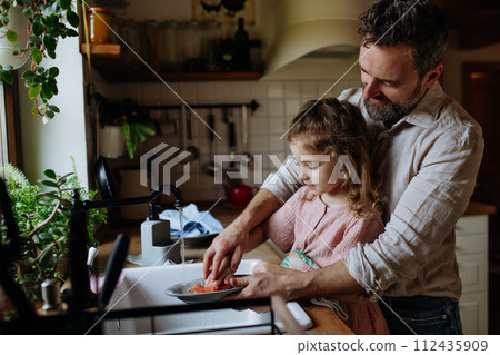 Dad and daughter washing dishes in sink together. Girls dad. Unconditional paternal love, Father's Day concept. Dad and daughter washing dishes in sink together. Girls dad. Unconditional paternal love, Father's Day concept. 112435909