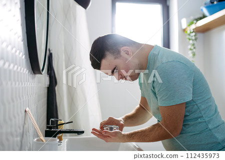 Young man with down syndrome learning how to shave, applying after shave lotion on face. Young man with down syndrome learning how to shave, applying after shave lotion on face. 112435973