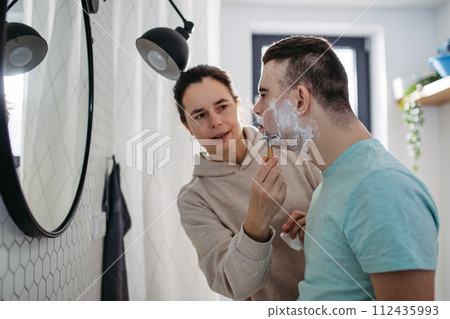 Mother applying shaving foam on son's face. Young man with down syndrome learning how to shave. Mother applying shaving foam on son's face. Young man with down syndrome learning how to shave. 112435993