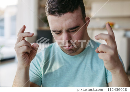 Young man with Down syndrome is focused, eyes closed. Disabled man making a wish, hoping for something. 112436028