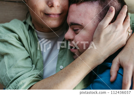 Portrait of young man with Down syndrome with his mother at home, holding, touching with foreheads. Concept of love and parenting disabled child. Close up. 112436037
