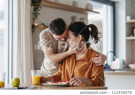 Young man with Down syndrome serving breakfast to his mother as a Mother's Day gift. Concept of Mother's Day and maternal love to disabled children. 112436078