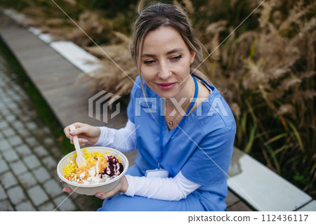 Nurse having healthy lunch in front of hospital building, taking break from work. Importance of breaks in healthcare. 112436117