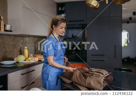 Female doctor getting ready for work, packing backpack, leaving house in scrubs with backpack. Work-life balance for healthcare worker. 112436122