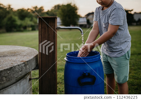 Boy washing his hands with water from a well. Well with a pump for outdoor washing in garden. 112436225