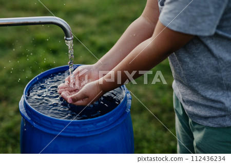 Boy washing his hands with water from a well. Well with a pump for outdoor washing in garden. 112436234