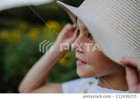 Beautiful young girl standing in front of sunflowers on field. Girl enjoying a beautiful flowers in the summer farm fields. Future female farmer. Beautiful young girl standing in front of sunflowers on field. Girl enjoying a beautiful flowers in the summer farm fields. Future female farmer. 112436255
