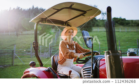 Progressive female farmer driving tractor on her own farm. 112436268