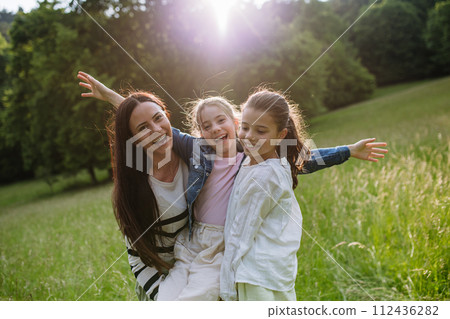 Beautiful mother with two daughters, playing at meadow, laughing, having fun. Concept of Mother's Day, maternal love. 112436282