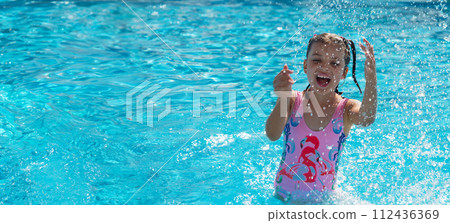 Portrait of happy laughing and playing with water spray 7 years old girl in swimming pool on sunny day 112436369