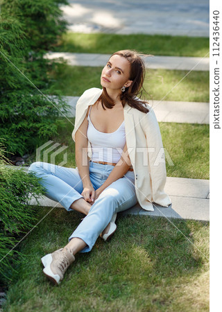 Stylish young woman at light casual outfit standing near the gray wall of the modern building. 112436440