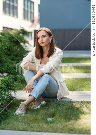 Stylish young woman at light casual outfit standing near the gray wall of the modern building. 112436441