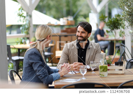 Couple sitting outdoors on terrace restaurant, having dinner date. Business lunch for two managers, discussing new business project. 112436708