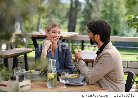 Couple sitting outdoors on terrace restaurant, having dinner date. Business lunch for two managers, discussing new business project. 112436712