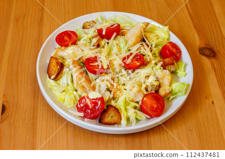 Fresh healthy caesar salad with chicken breast, cherry tomatoes, lettuce, parmesan cheese, dressing and croutons on wooden table Fresh healthy caesar salad with chicken breast, cherry tomatoes, lettuce, parmesan cheese, dressing and croutons on wooden table 112437481