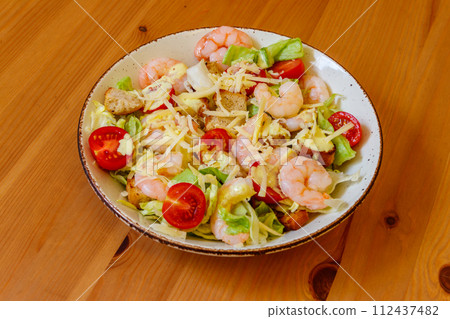 Fresh healthy caesar salad with prawns, cherry tomatoes, lettuce, parmesan cheese, dressing and croutons on wooden table Fresh healthy caesar salad with prawns, cherry tomatoes, lettuce, parmesan cheese, dressing and croutons on wooden table 112437482