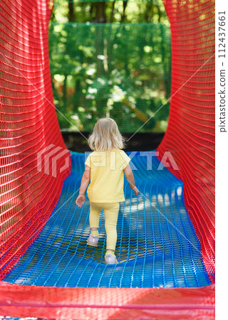 Little girl having fun at a rope playground. The girl is playing on net ropes. 112437661