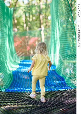 Little girl having fun at a rope playground. The girl is playing on net ropes. 112437664