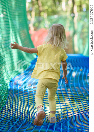 Little girl having fun at a rope playground. The girl is playing on net ropes. 112437665