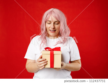 Portrait of cheerful, happy woman receive gift, smiling excited. Girl with pink hair holding wrapped present on red background. Valentine's Day Women's Day birthday holiday concept. 112437731