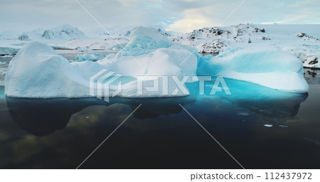 Global warming, melting icebergs in Antarctica. Glacier with melted cavity floating in blue ocean water. Polar climate change at sunny winter day. Cinematic ecology scene. Close up shot 112437972