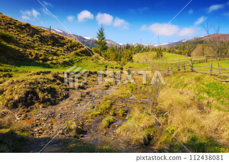 mountainous rural landscape of ukraine with grassy fields behind wooden fence. carpathian countryside scenery in spring on a sunny morning 112438081