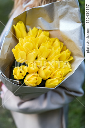 Someone holding bouquet of yellow flowers in craft paper. Fresh yellow tulips. Vertical frame. 112439167