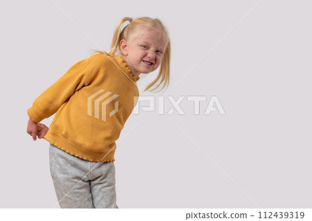 Portrait of a little capricious girl in a yellow sweater on a white background 112439319