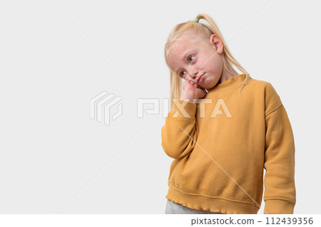 Portrait of sad little girl with blond hair in a yellow sweater on a white background. Portrait of sad little girl with blond hair in a yellow sweater on a white background. 112439356