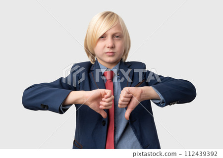 Displeased young man with blond hair, wears blue jacket and red tie, shows thumbs down, has dissatisfied expression, isolated over white background. Negative human emotions, facial expressions Displeased young man with blond hair, wears blue jacket and red tie, shows thumbs down, has dissatisfied expression, isolated over white background. Negative human emotions, facial expressions 112439392