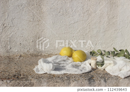 Wedding still life. Fresh lemons fruit, eucalyptus tree branches, ribbon and muslin textile in sunlight. White shabby old textured wall background. Vacation concept. Mediterranean summer banner. 112439643
