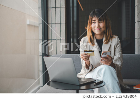 Mobile Shopping. Cheerful woman using smartphone shopping online holding credit card making payment sitting on sofa at home. Internet banking application and e-commerce. Mobile Shopping. Cheerful woman using smartphone shopping online holding credit card making payment sitting on sofa at home. Internet banking application and e-commerce. 112439804