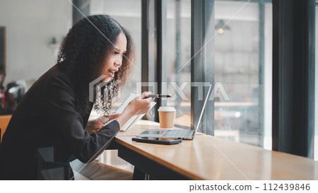 Business analytics concept, Businesswoman working diligently on a laptop at coworking space desk, immersed in managing her professional tasks. 112439846
