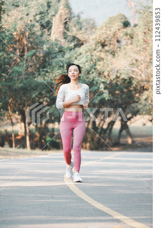 Full body female athlete in activewear running on road path during cardio workout on sunny summer day in park. Full body female athlete in activewear running on road path during cardio workout on sunny summer day in park. 112439853