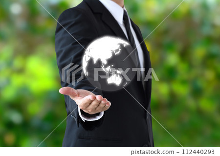 A businessman holding up the globe with fresh greenery in the background 112440293