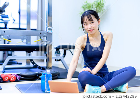 A young woman trains her body at a personal gym, watches videos on a tablet, looks at how to train, looking at camera 112442289