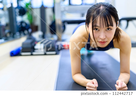 Young woman training her body at a personal gym, muscle training girl, push-up, plank, front view Young woman training her body at a personal gym, muscle training girl, push-up, plank, front view 112442717