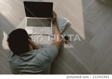 Top view of asian man using computer, lying on floor while working on laptop with coffee and typing keyboard, relaxing living alone at apartment. 112442891