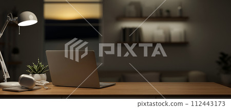 A back view image of a laptop computer on a wooden table in a modern dark living room at night. 112443173