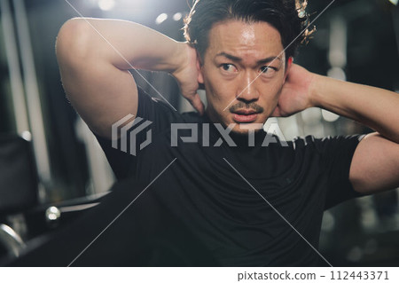 堅忍的年輕人在訓練館裡表情嚴肅地做仰臥起坐 112443371