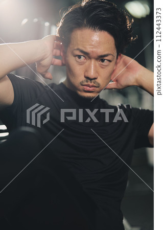 Stoic young man doing sit-ups with a serious expression at the training gym 112443373