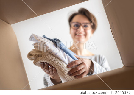 Donation concept. A woman puts clothes in a cardboard box at home for donation, recycling Donation concept. A woman puts clothes in a cardboard box at home for donation, recycling 112445322